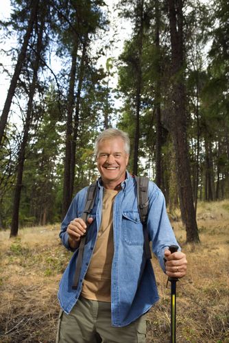 Smiling hiker in blue shirt and backpack holding walking poles in a pine forest