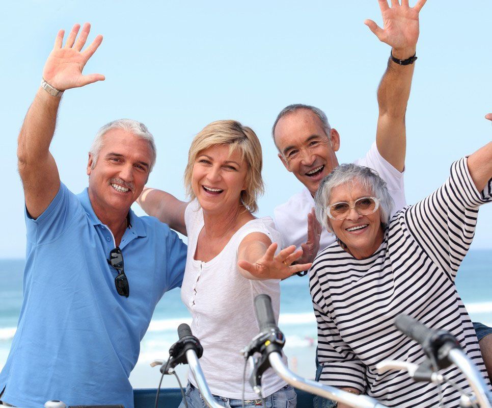 Four smiling people waving from bicycles against a bright blue sky