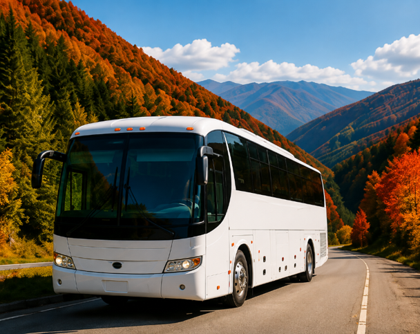White coach bus on a mountain road with autumn trees and distant blue peaks