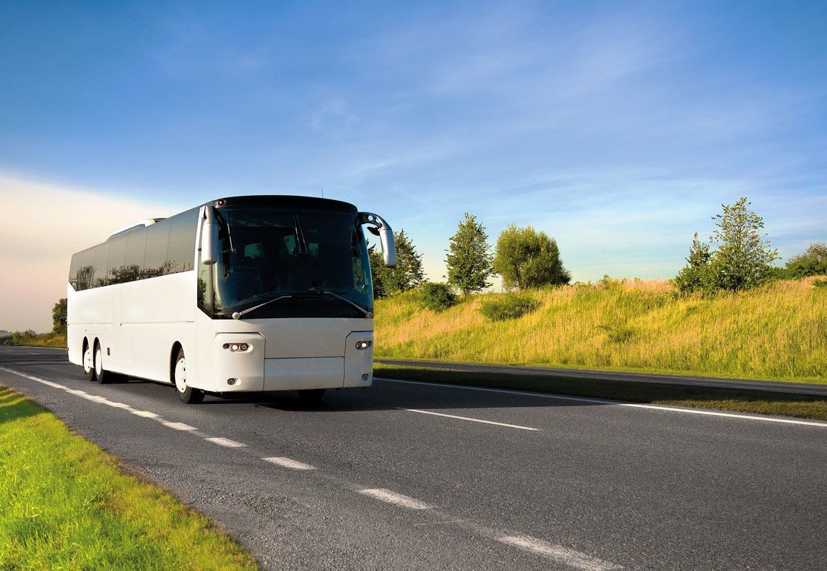White coach bus driving on a rural highway under a blue sky