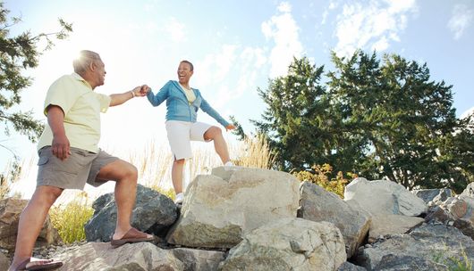 Two hikers helping each other climb rocks on a sunny trail