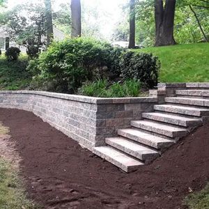 A stone wall with stairs leading up to it in a backyard.