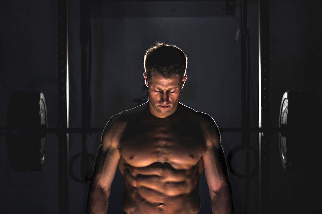 A shirtless man is standing in a dark room with his eyes closed.