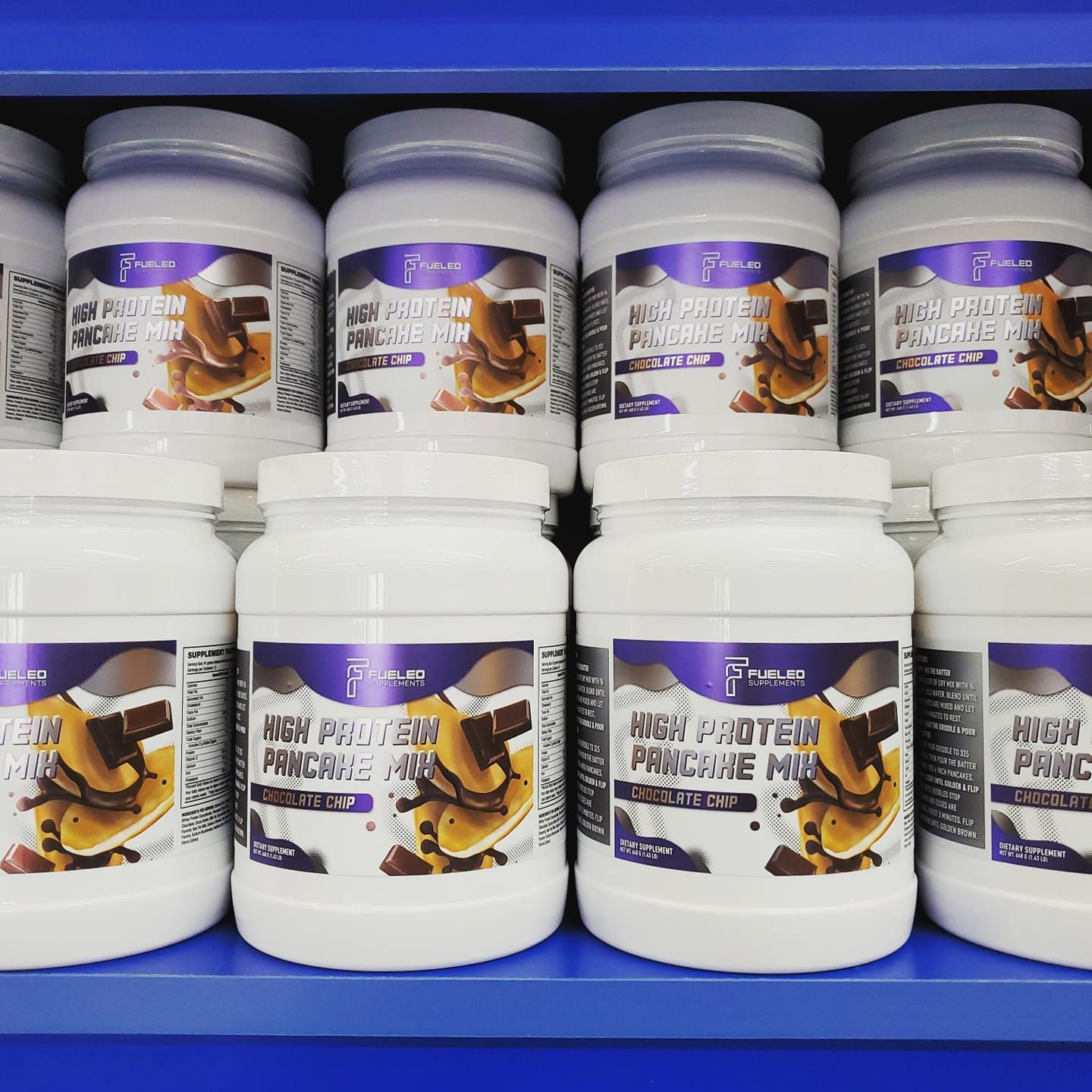 Several jars of high protein pancake mix are lined up on a blue shelf.