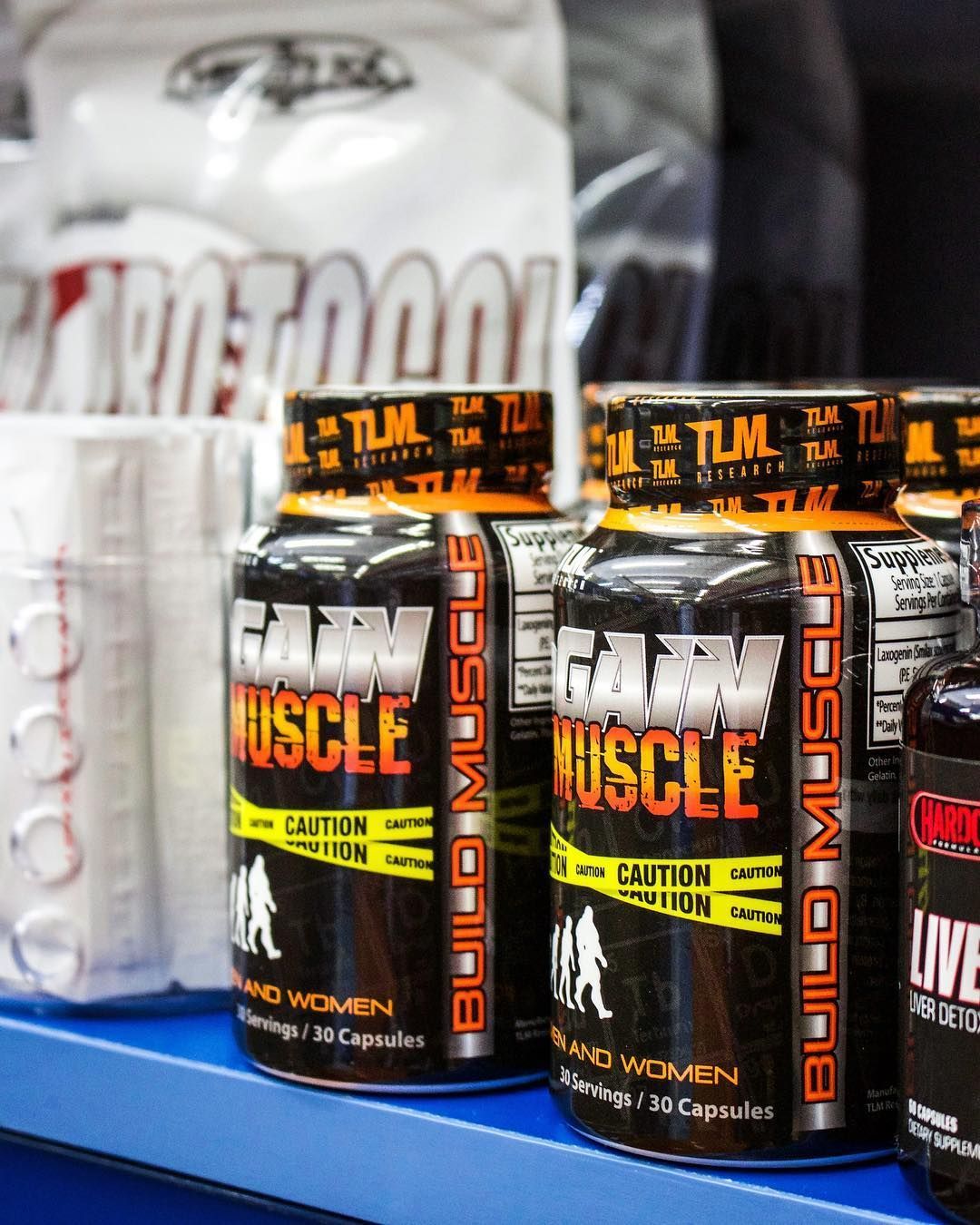 Several bottles of build muscle sit on a blue shelf.