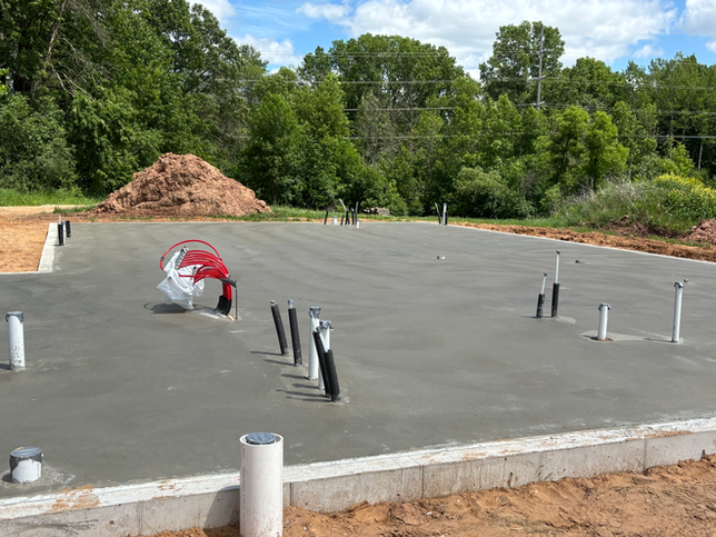 Fresh concrete foundation slab for a new building, featuring plumbing pipes protruding from the surface.