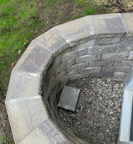 A curved basement window well made of stacked grey concrete blocks filled with gravel.