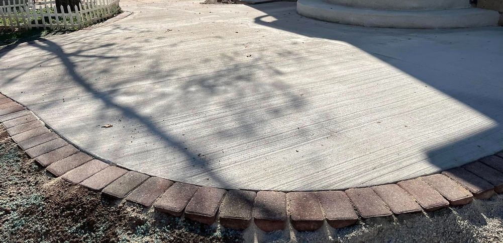 A semicircular concrete patio bordered by reddish-brown pavers, with tree shadows cast across the textured surface.