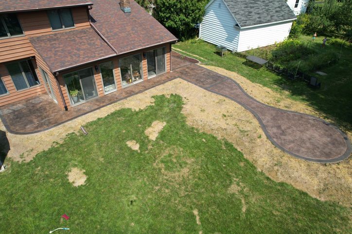 Aerial view of a house with a newly installed brown concrete patio and a curved walkway extending into the backyard lawn.