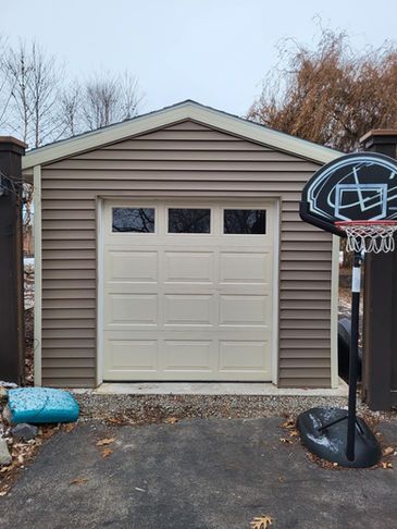 A beige, single-car garage with white trim and a basketball hoop in the foreground on a paved driveway.