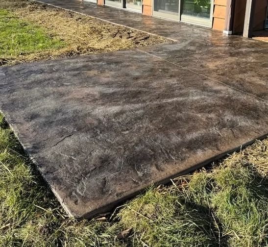 A dark, textured stamped concrete patio extends from a house into a grassy yard.