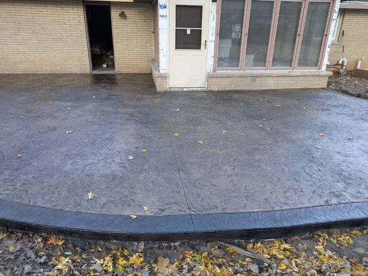 A stamped grey concrete patio with a dark border, located outside a home with a brick exterior.
