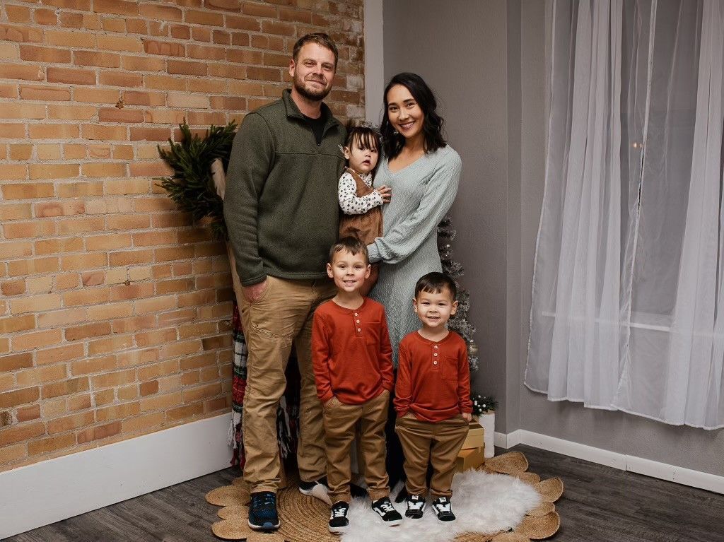 A family of five posing for a portrait in front of a brick wall, wearing sweaters and casual clothes.