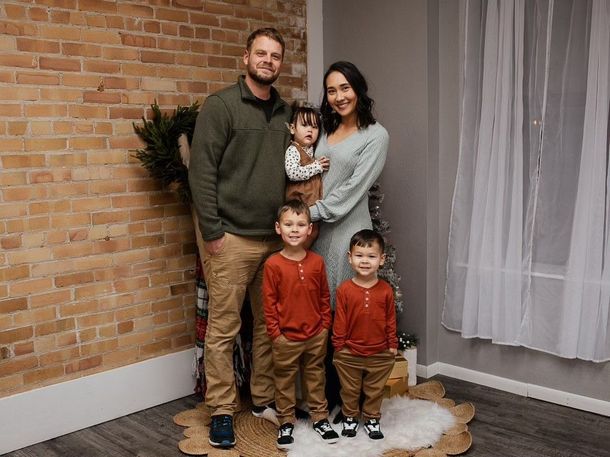 A family of five posing for a portrait in front of a brick wall, wearing sweaters and casual clothes.