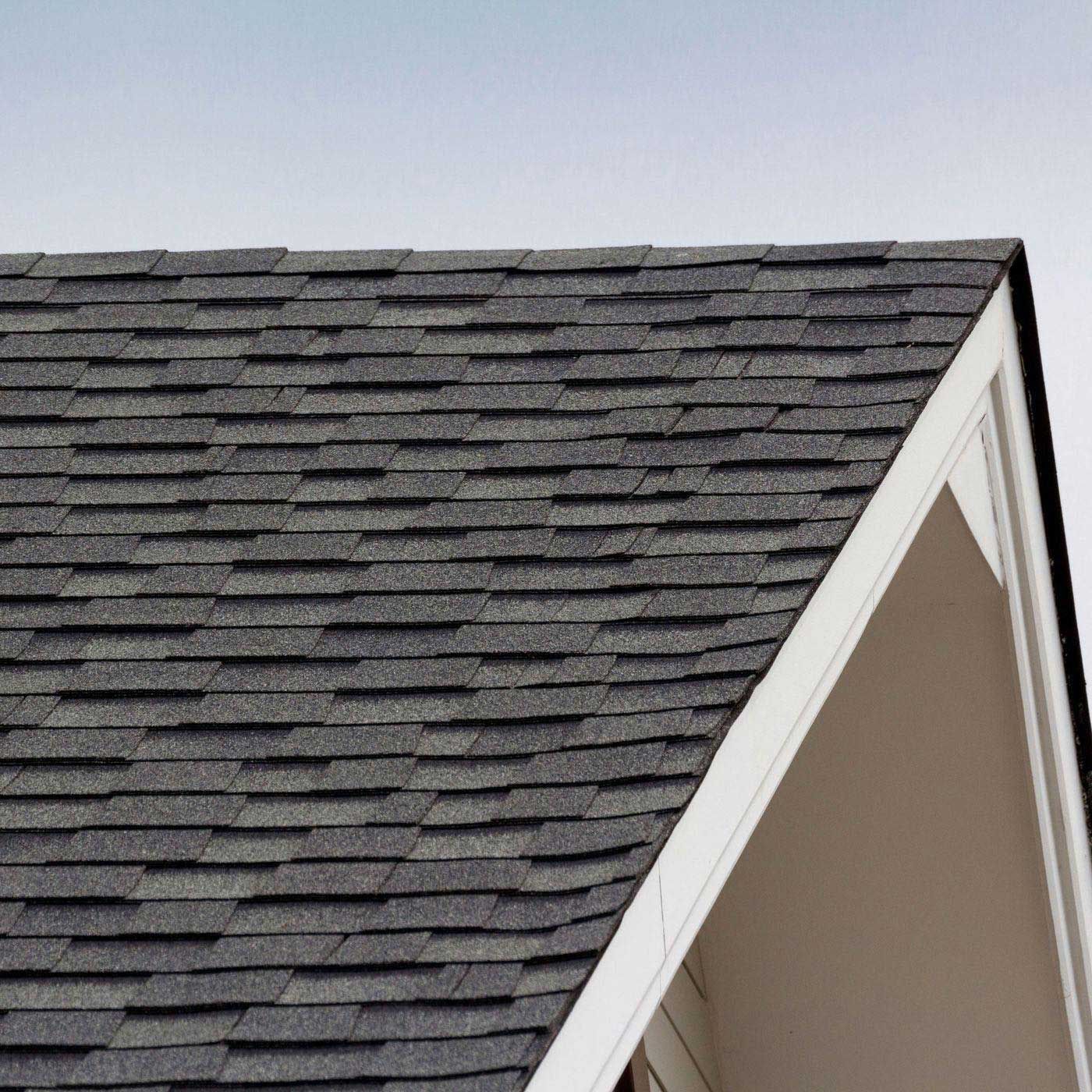 Close-up view of a dark gray shingle roof with a white-trimmed gable against a pale blue sky.