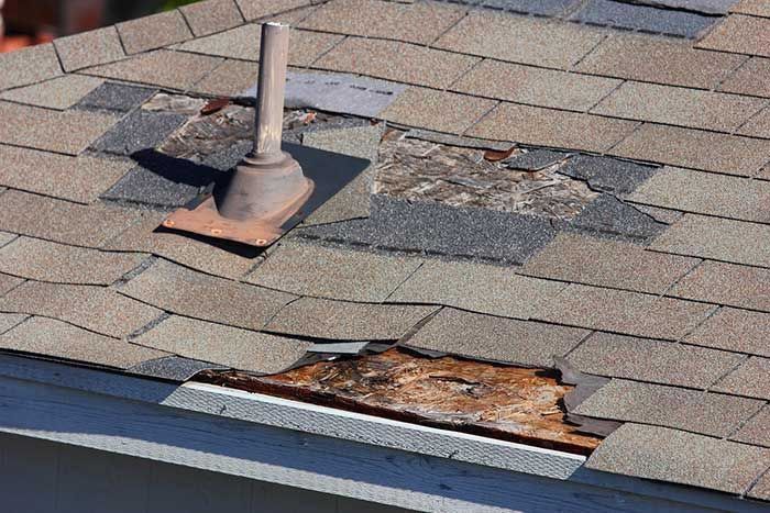 Damaged asphalt shingle roof with missing and deteriorated sections, including near a vent.