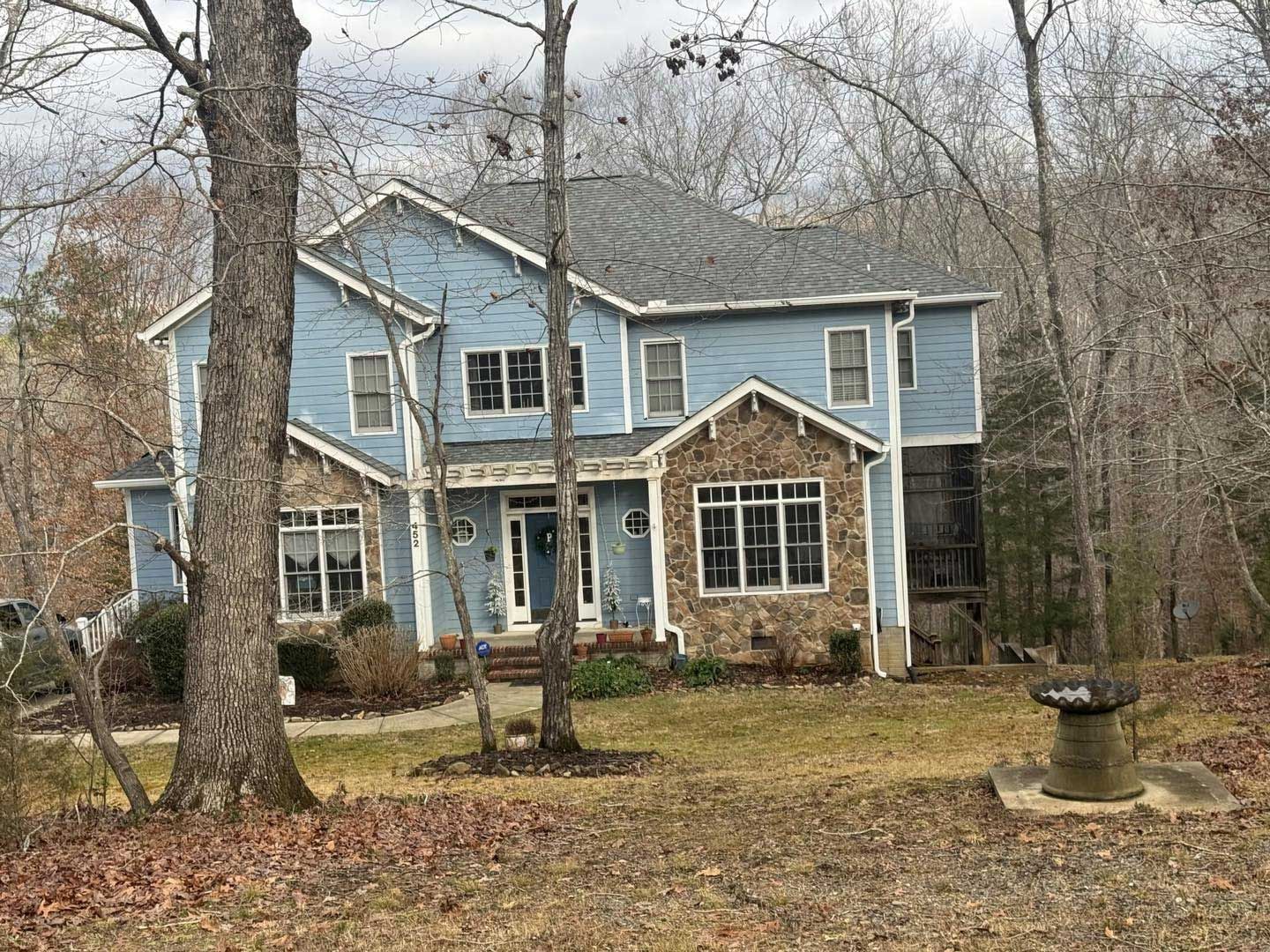 Two-story blue house with stone accents on a hill surrounded by trees in the autumn.