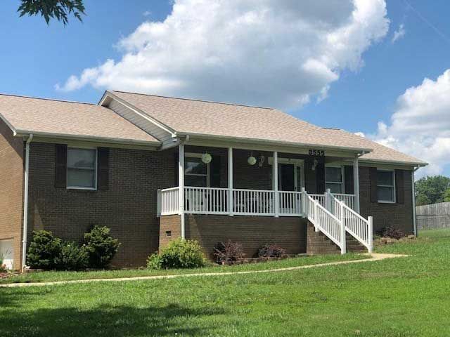 Brick house with a white porch, railing, and steps. Green lawn and blue sky with clouds.