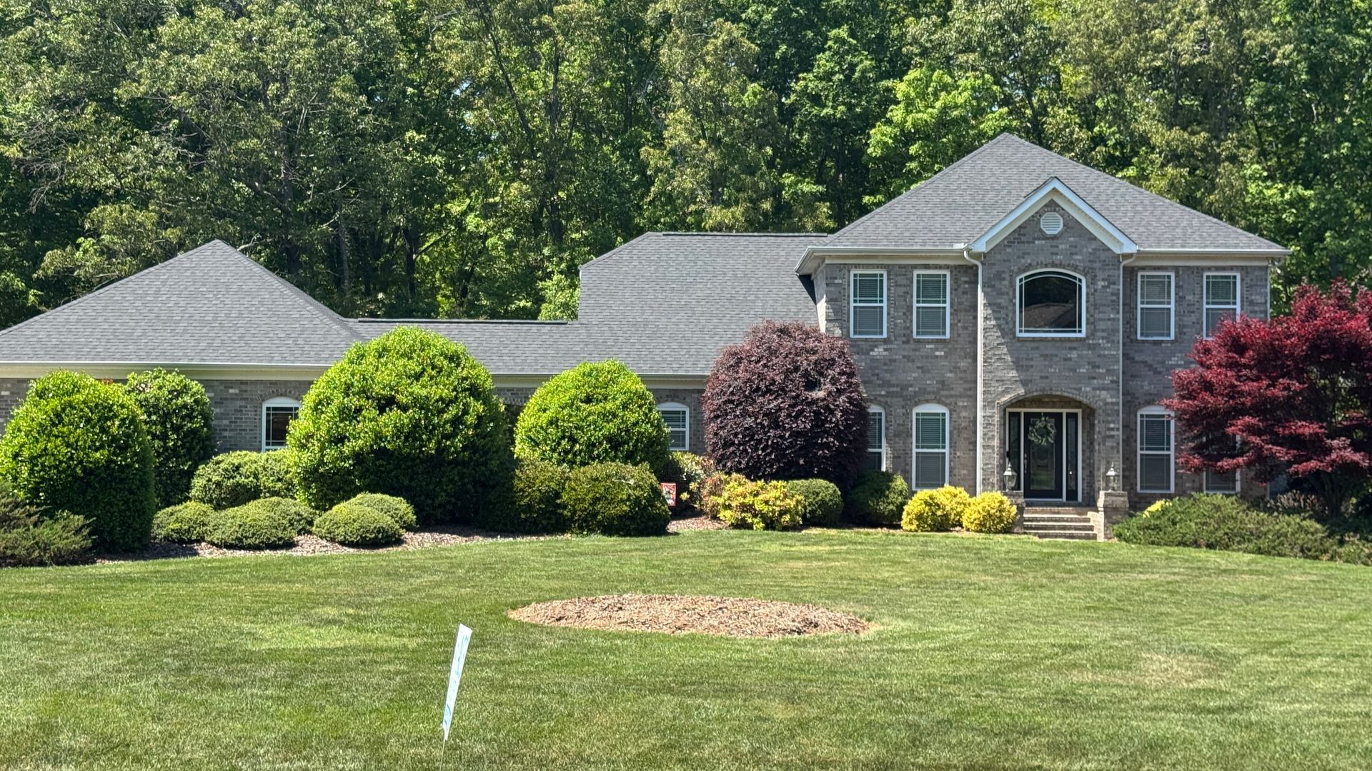 Suburban house with manicured lawn, trimmed shrubs, and trees in the background