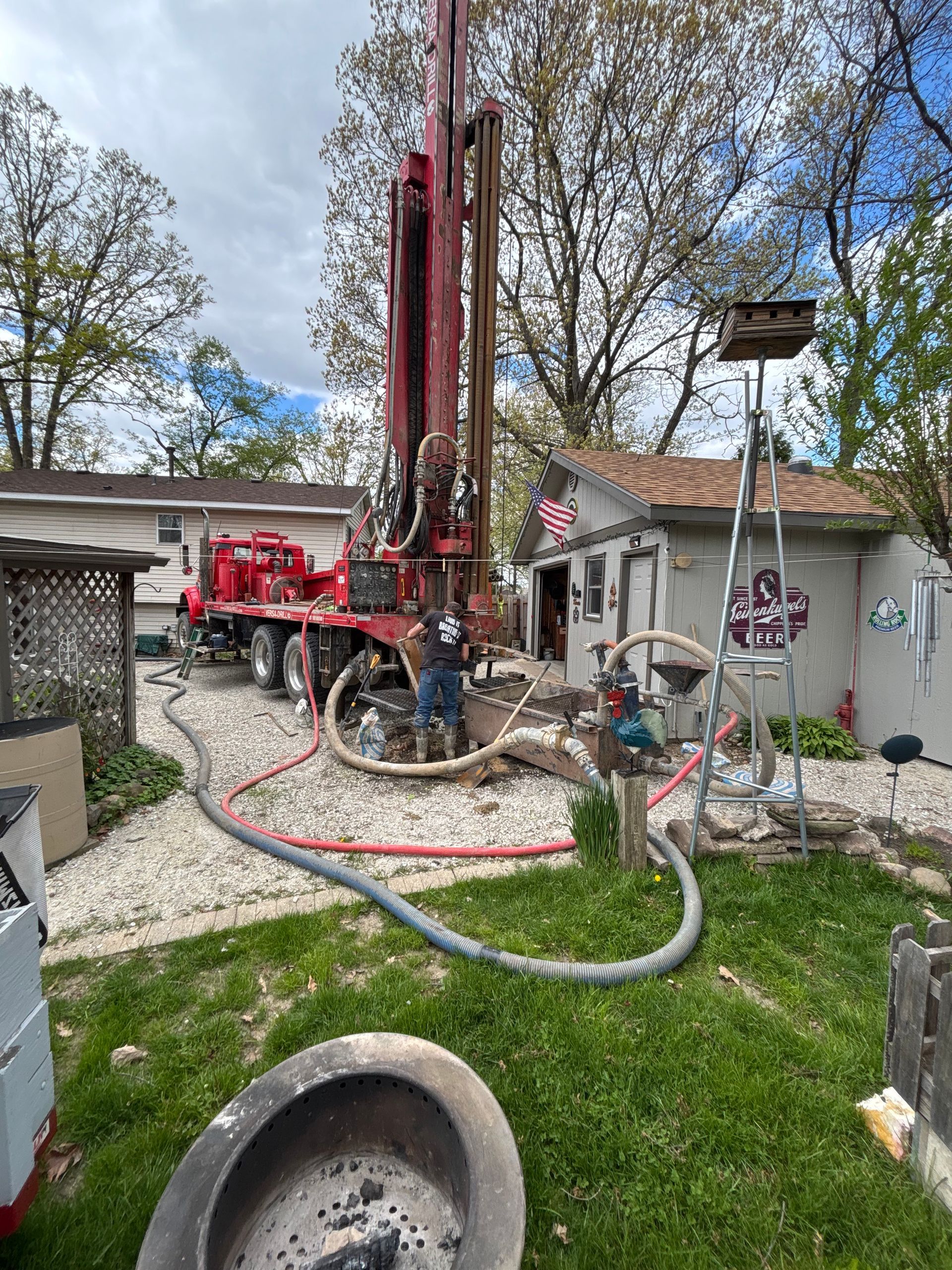 Drilling rig beside a house, with hoses and equipment set up in a residential yard