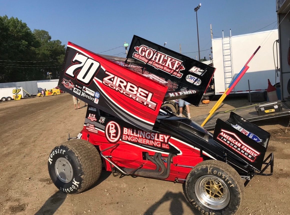 a red race car with the number 20 on the side is parked in a dirt field