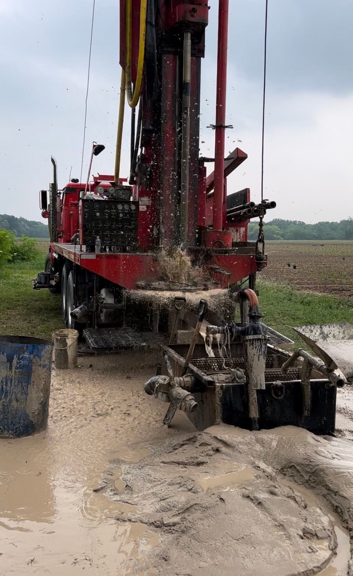 a red truck is drilling a hole in the ground in a muddy field