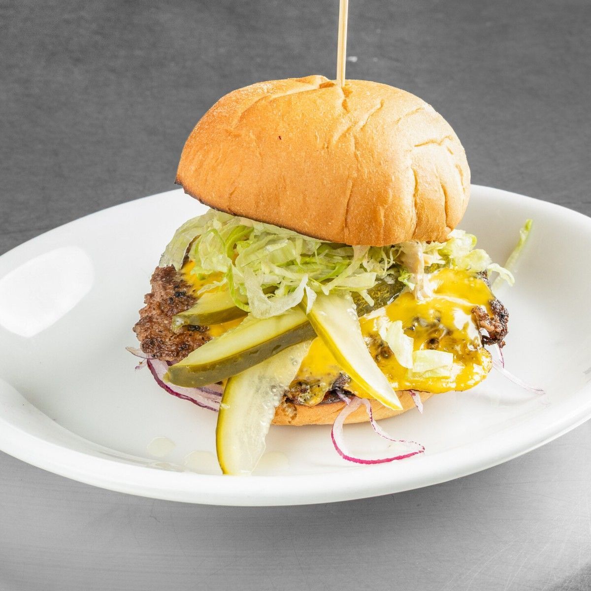 Cheeseburger on a white plate with lettuce, cheese, and onion under a bun on a gray background