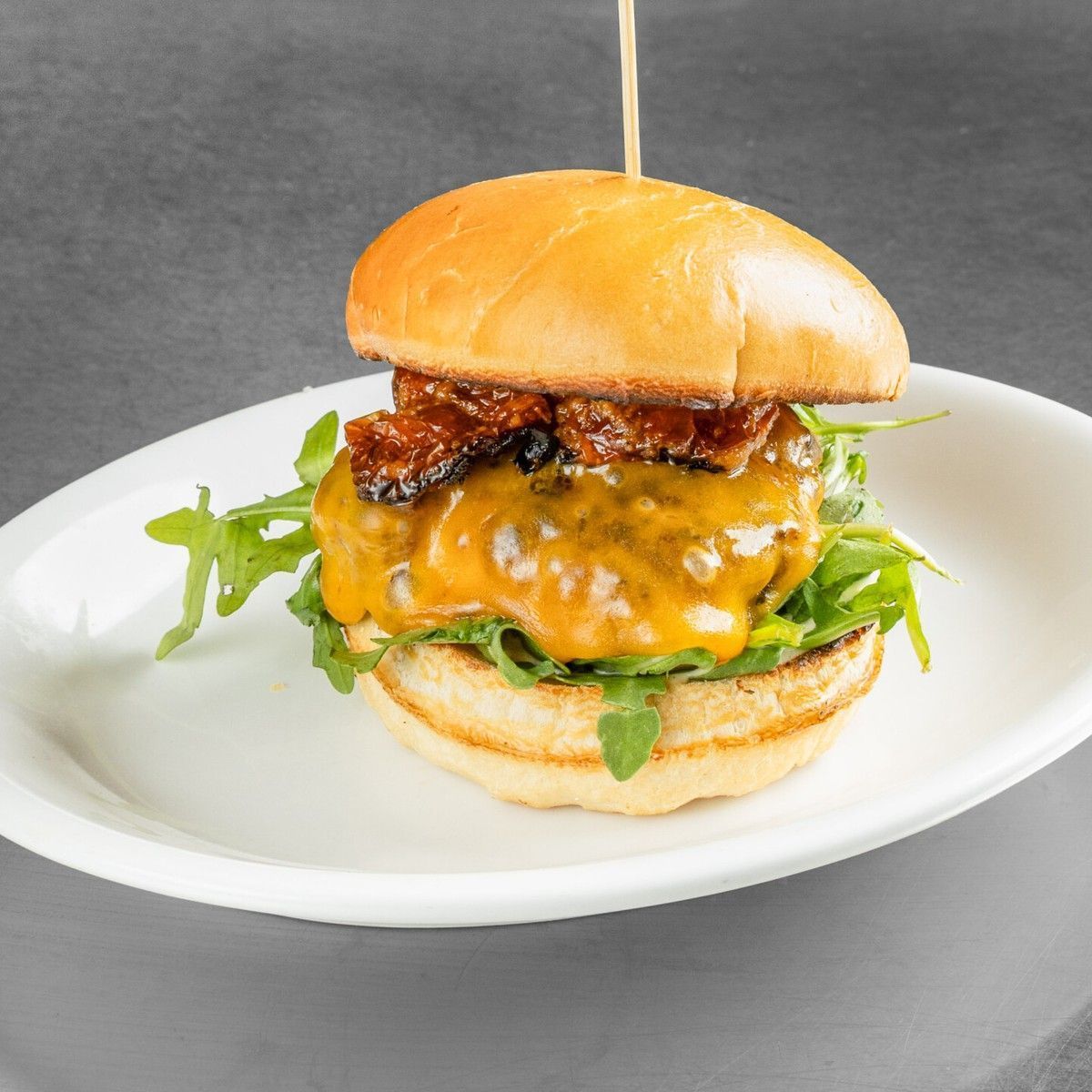 Cheeseburger with melted cheese on a white plate against a gray background