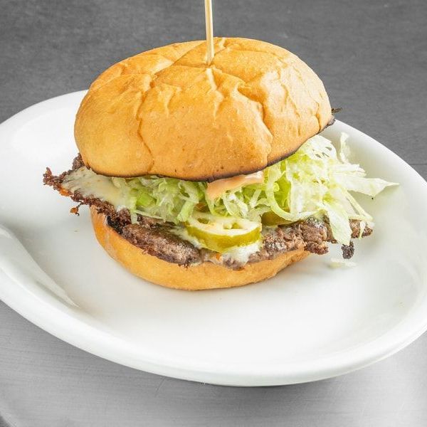 Beef burger on a white plate with lettuce, pickles, and cheese on a gray background