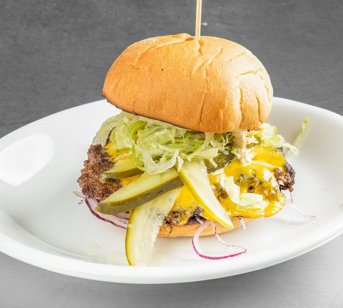 Hamburger on a white plate with pickles, shredded lettuce, and melted cheese.