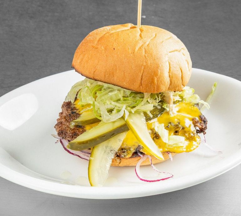 Hamburger on a white plate with pickles, shredded lettuce, and melted cheese.