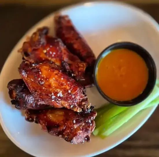 Glazed chicken wings with dipping sauce and celery on a white plate