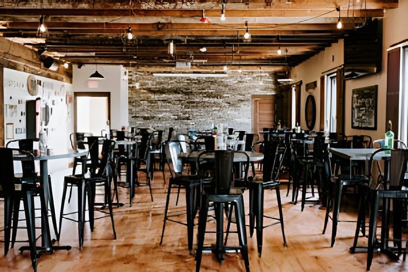Interior of a brewery or restaurant with tables and chairs, exposed brick and wooden beams.