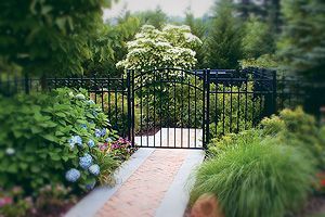 There is a brick walkway leading to a gate in the middle of a garden.