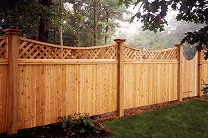 A wooden fence with a lattice design is surrounded by grass and trees.