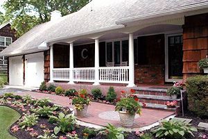 The front of a house with a porch and flowers in front of it.