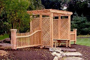 A wooden pergola with a bench and a fence.