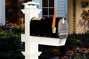 A black mailbox is sitting on top of a white post in front of a house.