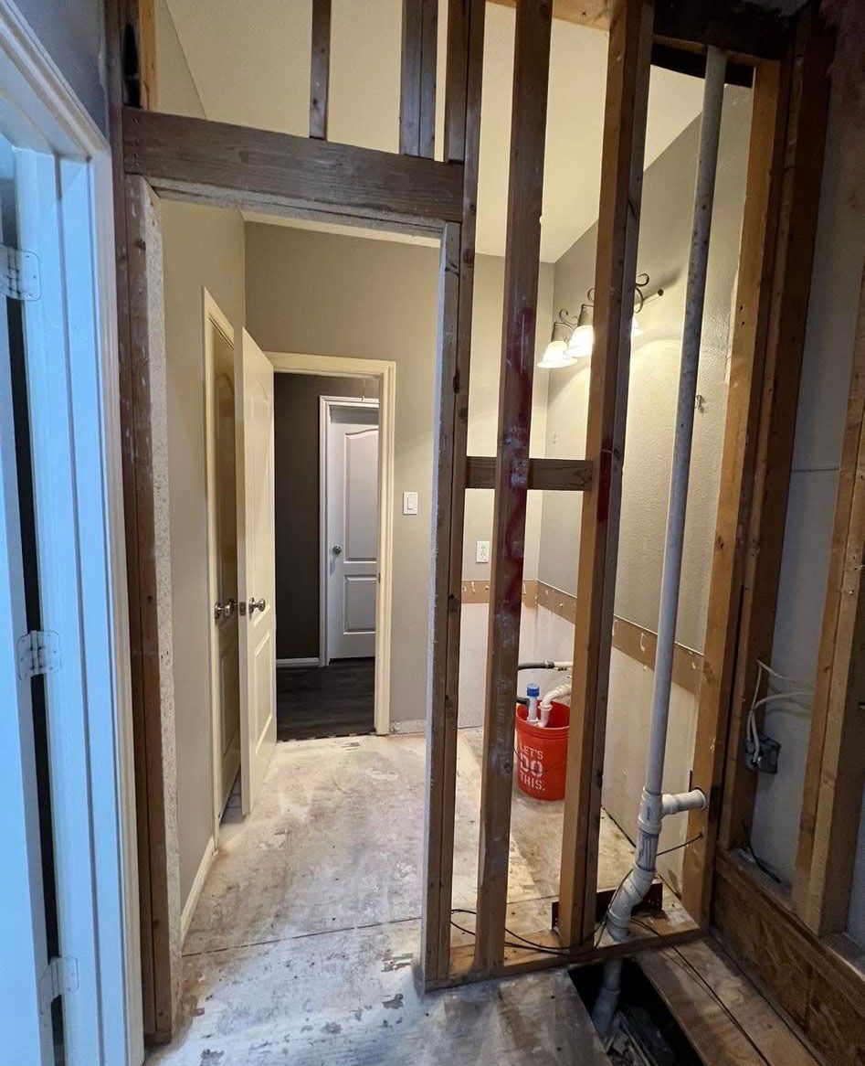 Interior view of a partially framed doorway and hallway, showing studs, drywall, plumbing, and a partially open door.