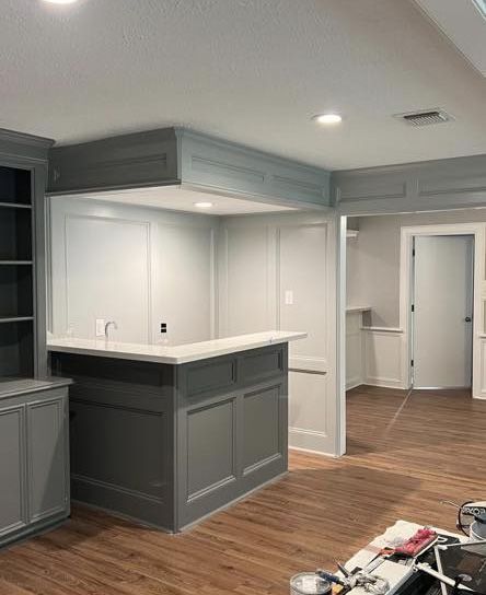 Gray home bar with white countertop and wood flooring.