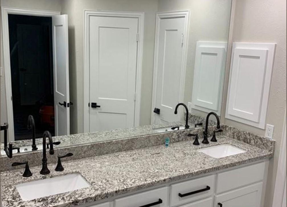 Bathroom with double sinks, granite countertop, white cabinets, black faucets, and large mirror.