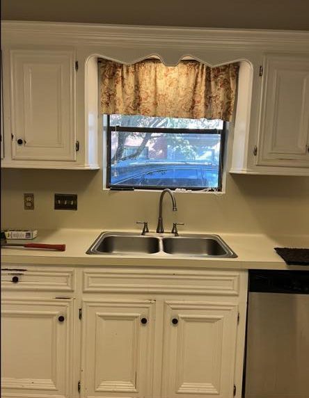 Kitchen sink and cabinets with a window above, featuring a brown curtain.