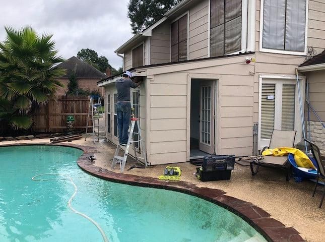 Construction workers on a ladder, working on a house with a pool in the backyard.