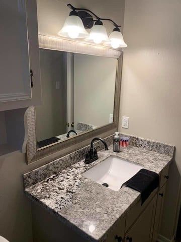 Bathroom vanity with a granite countertop, a mirror, and a three-light fixture.