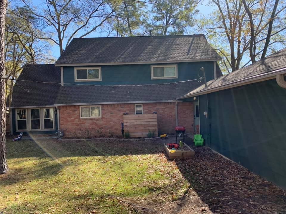 Backyard view of two-story house with green siding, brick, and attached garage; trees and grass in the yard.