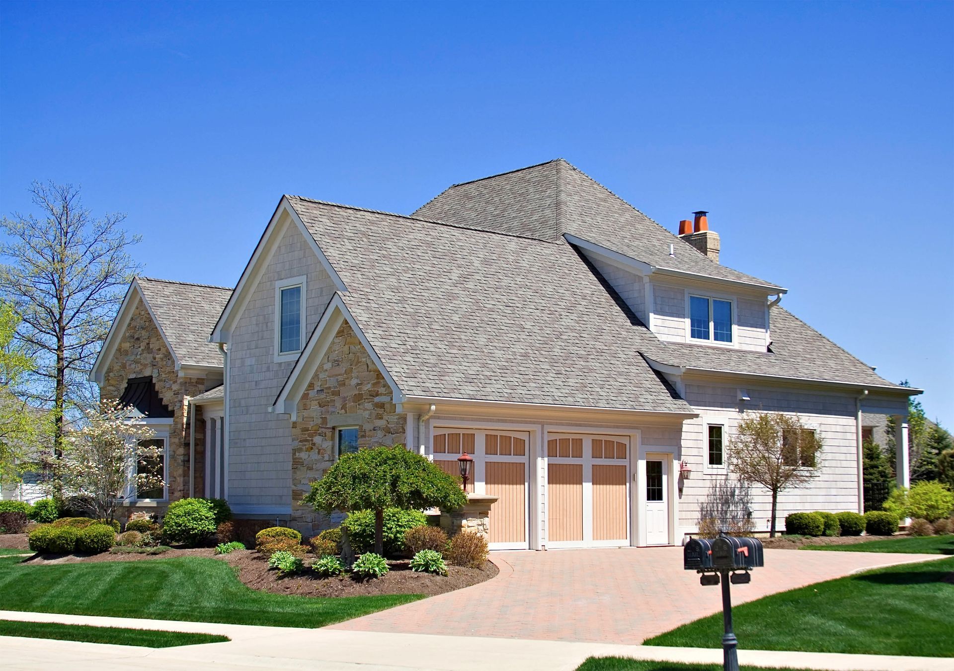 House with tan siding, stone accents, and a brick driveway on a sunny day.