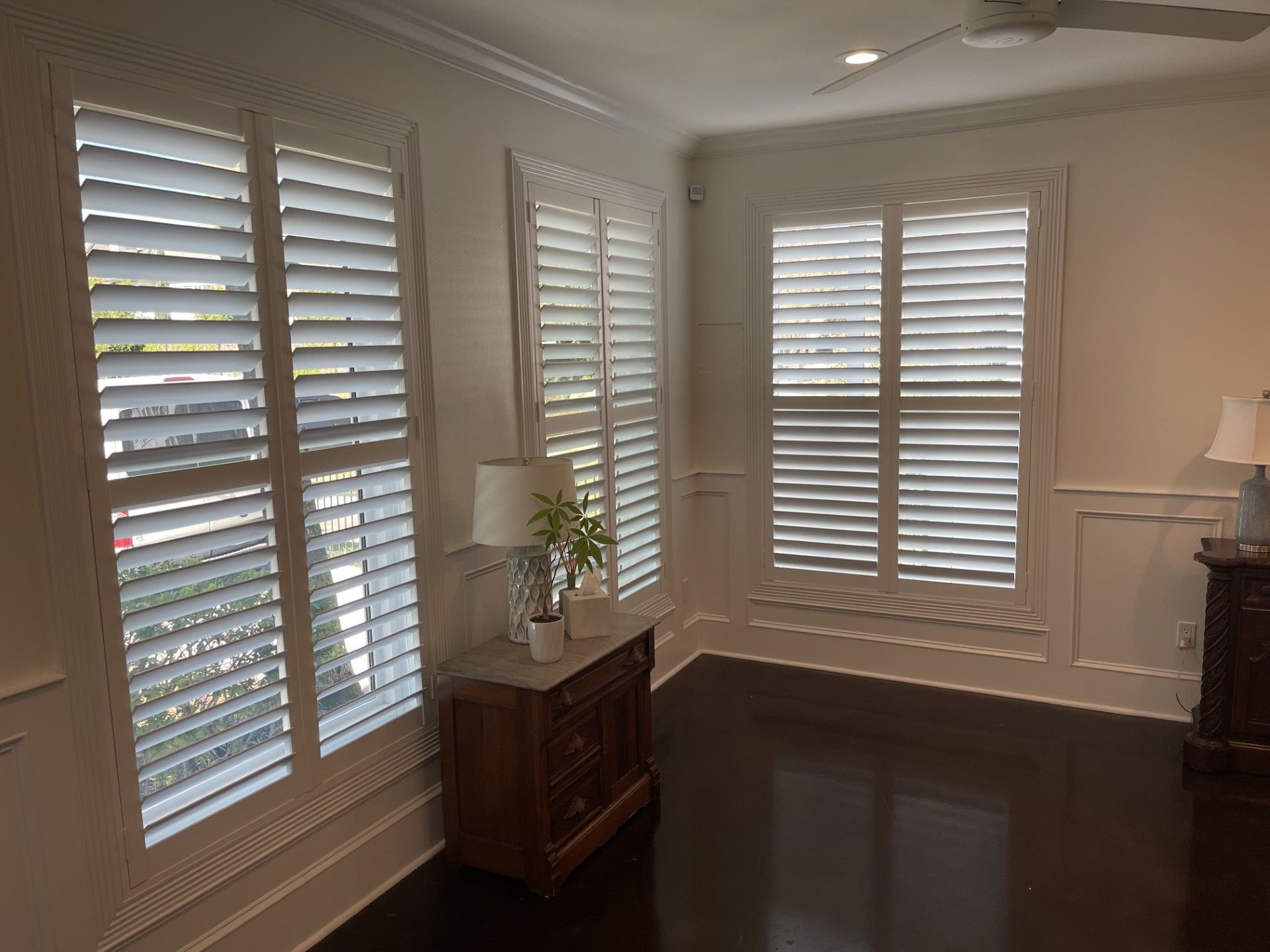 Room with three white shuttered windows, dark wood floor, and a wooden cabinet.