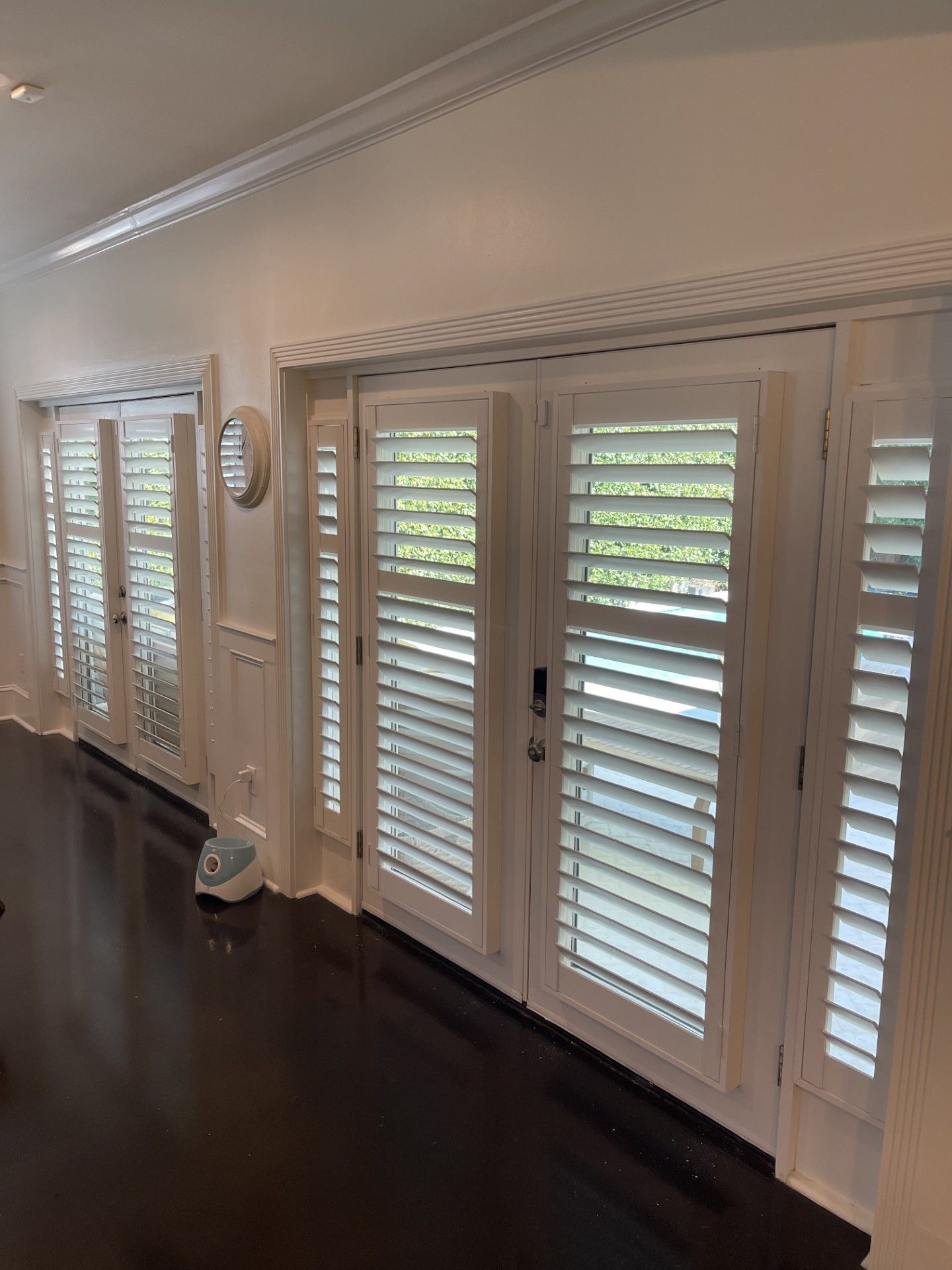 White shuttered doors and windows on dark wood floor, in a white-walled room.