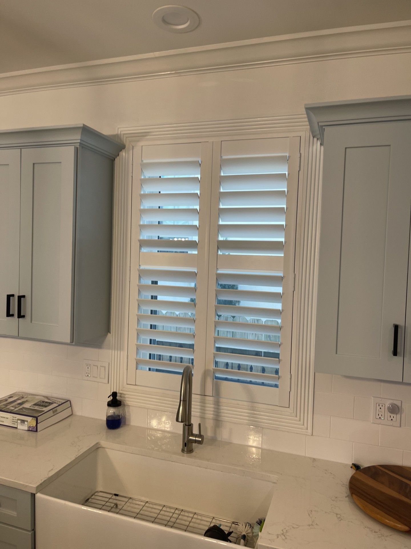 Kitchen window with white shutters, blue cabinets, and a white sink.