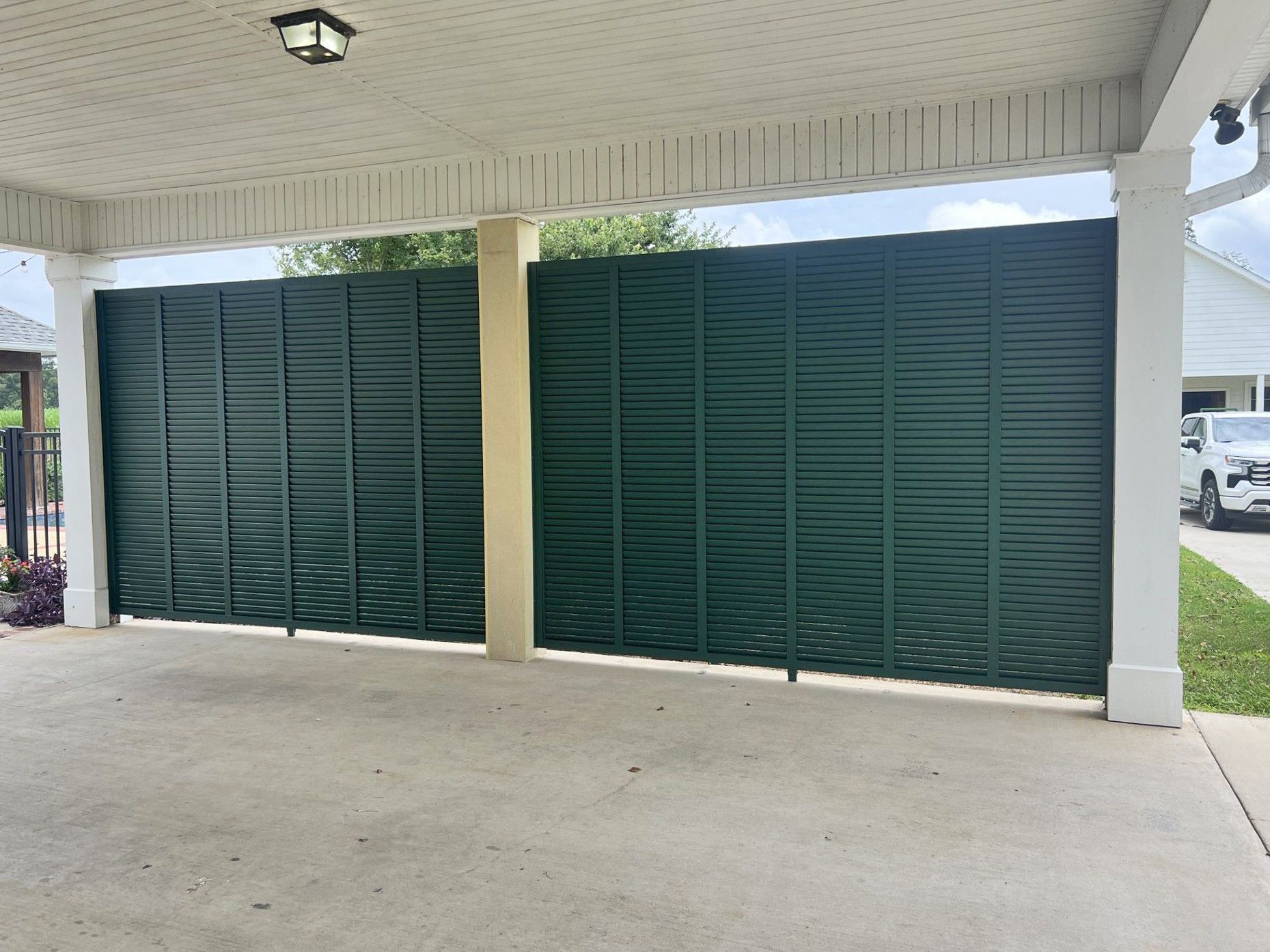 A carport with a green fence and a white car parked underneath it.